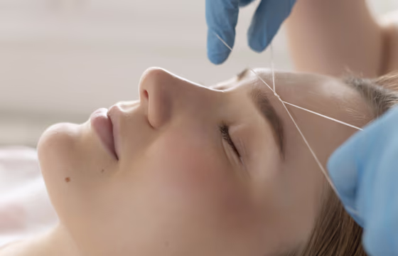 Profissional realizando depilação facial com linha na região da sobrancelha de cliente deitada