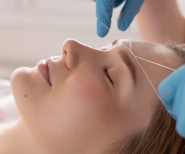 Depilação facial com linha egípcia sendo realizada por profissional em cliente deitada com olhos fechados