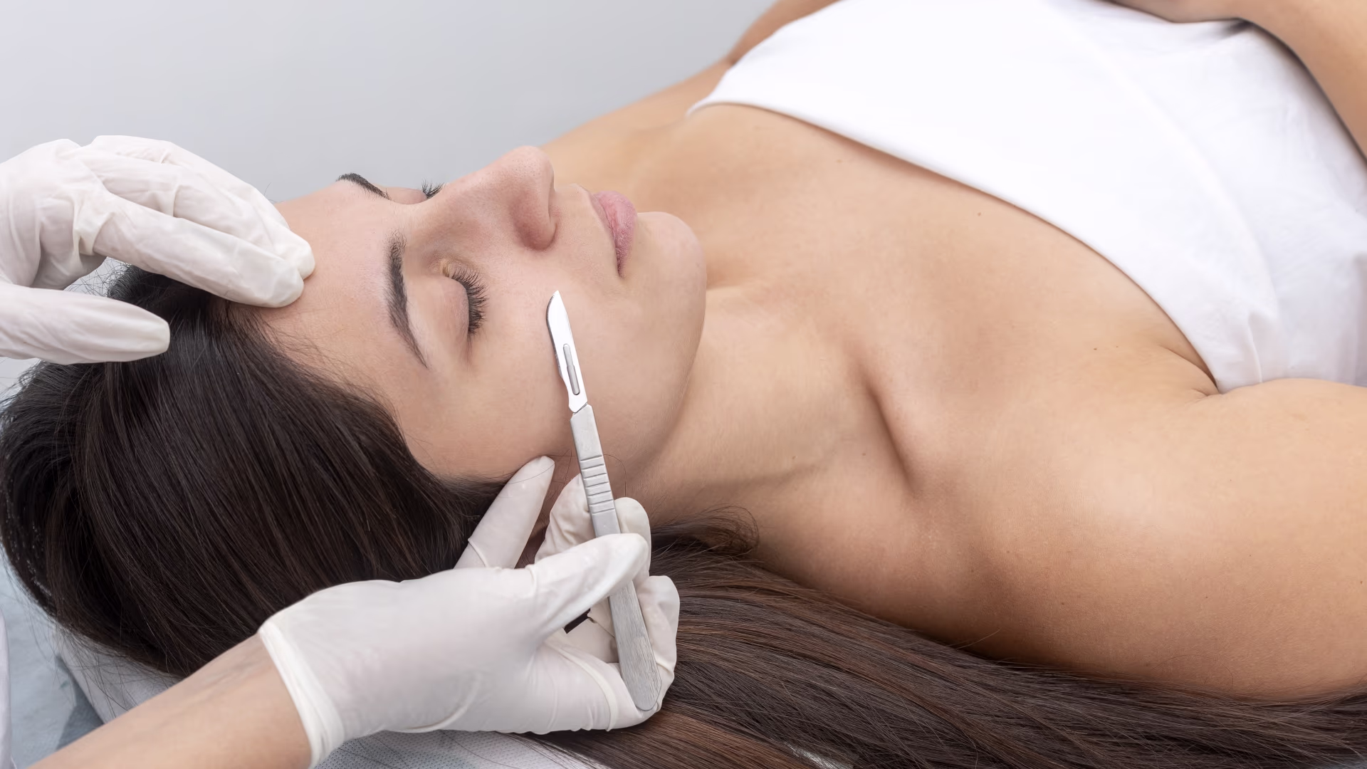 Profissional realizando dermaplaning com lâmina estéril no rosto de cliente em ambiente estético