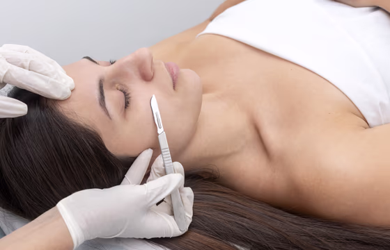 Profissional realizando dermaplaning com lâmina estéril no rosto de cliente em ambiente estético