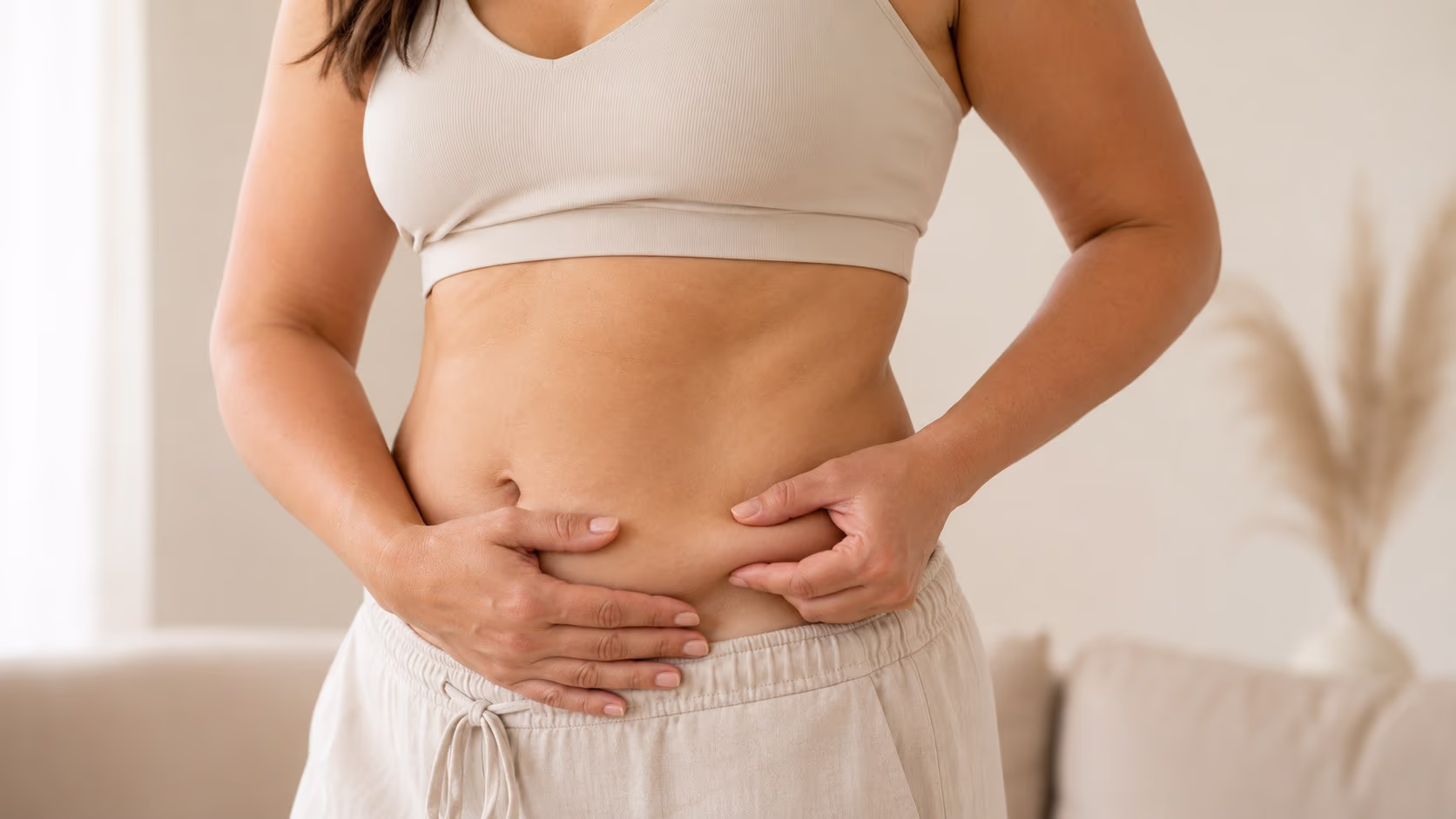 Mulher em roupa clara segurando a região abdominal, ilustrando cuidados com flacidez nos braços e abdômen