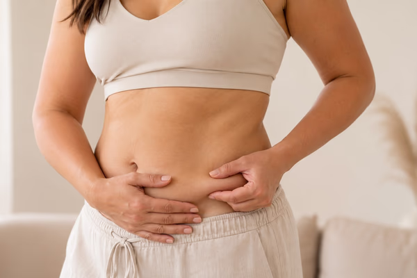 Mulher em roupa clara segurando a região abdominal, ilustrando cuidados com flacidez nos braços e abdômen