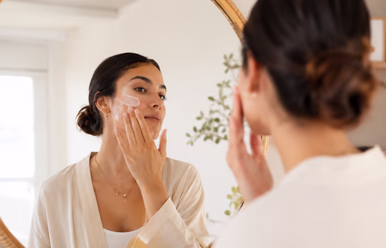 Mulher aplicando sérum cosmético no rosto diante do espelho, rotina de cuidado com GHK-Cu
